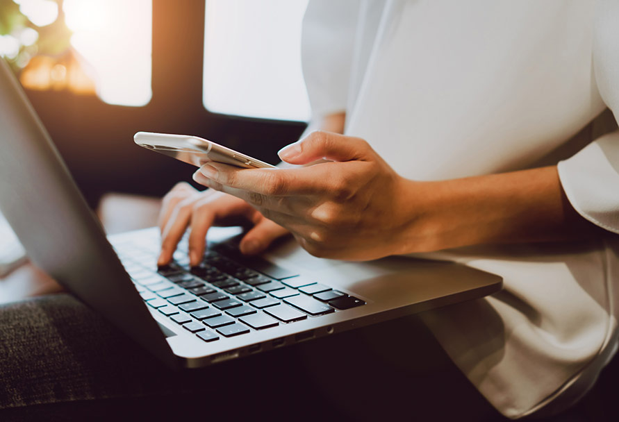 Close up of person using a laptop and cell phone