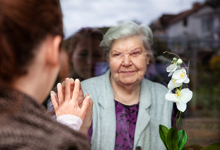 Elderly lady holding hand up to window