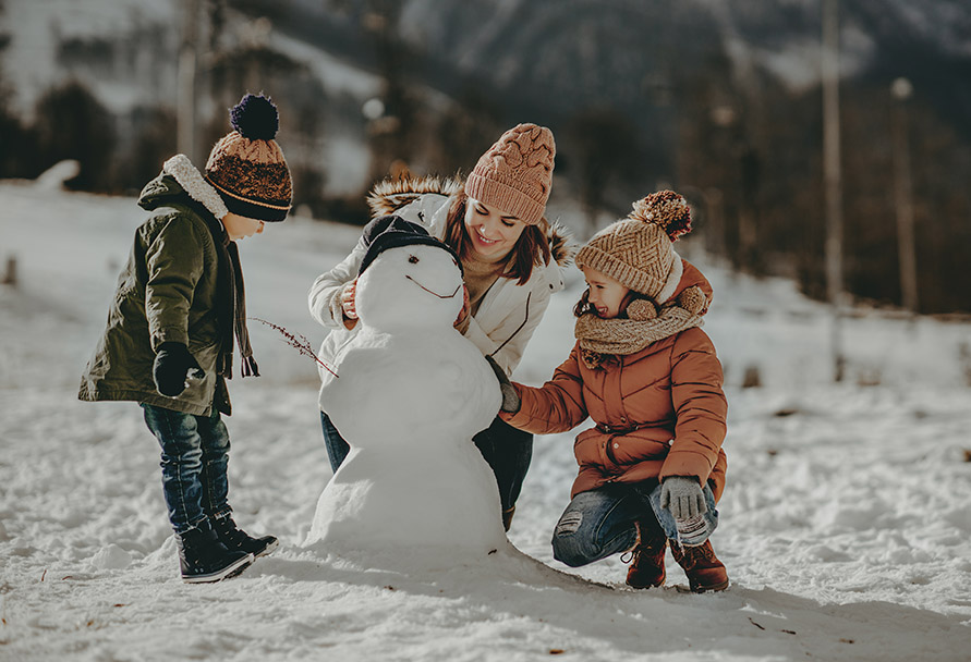 Woman building a snowman with two children