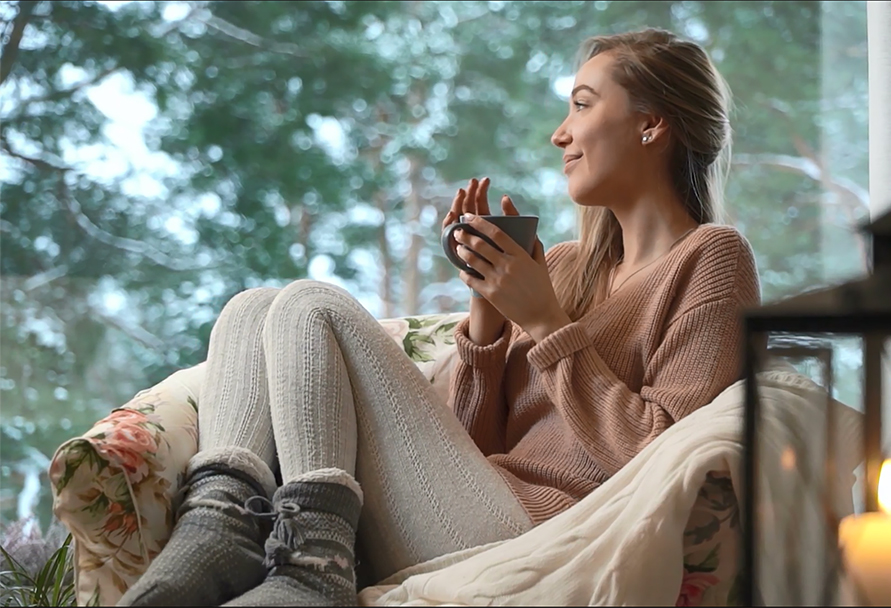 Woman with a hot beverage watching the snow outside the window