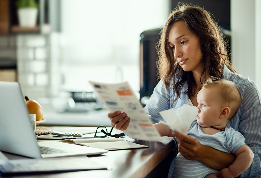 Woman holding a baby and looking at a paper bill