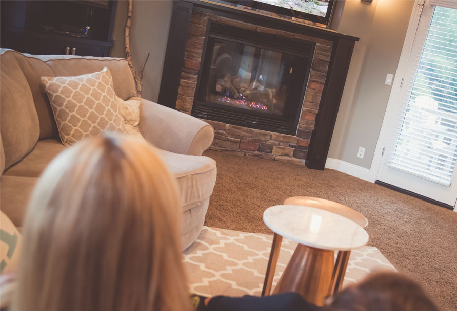 Back of a woman's head sitting in a living room with a fireplace in view