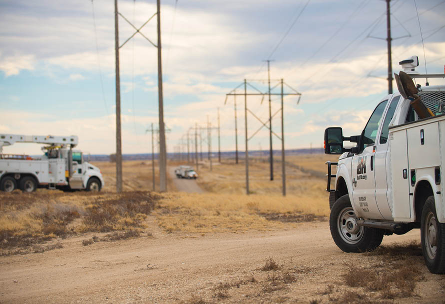 Service trucks on a dirt road with electric transmission lines
