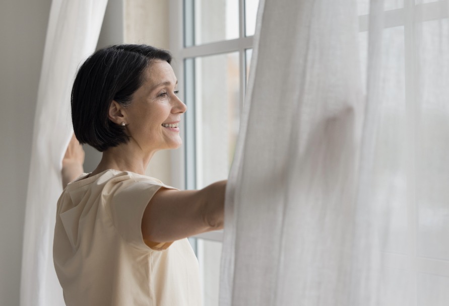 Woman opening window with white curtains