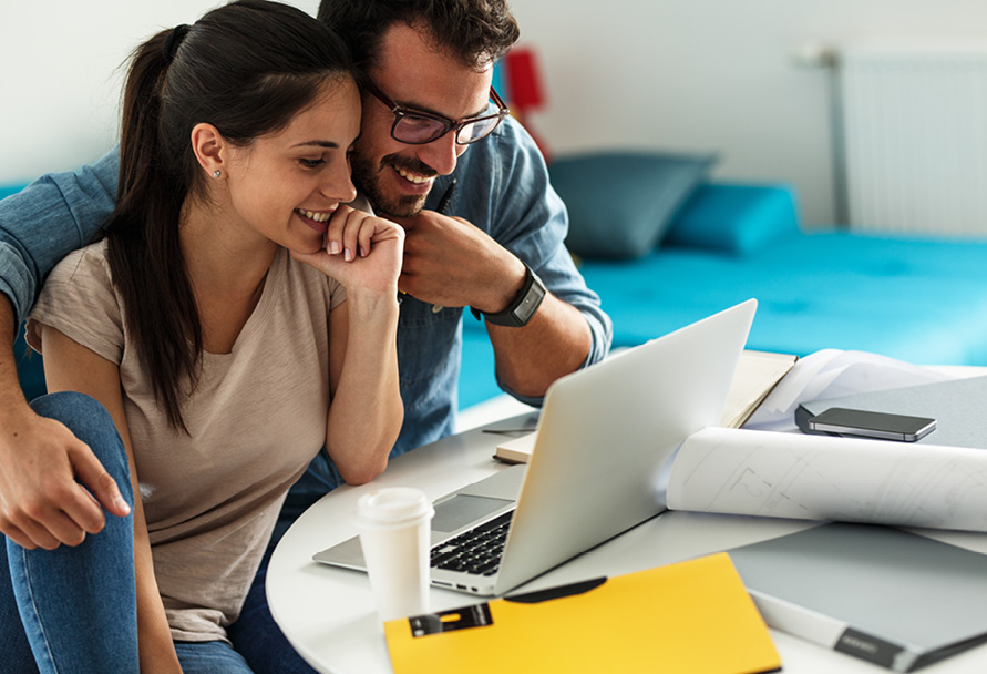 A couple sitting in front of a laptop computer in a living room