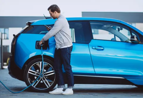 A man charging a blue electric vehicle