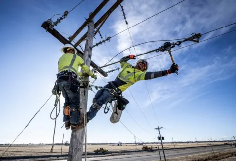 Two linemen working at the top of a power pole