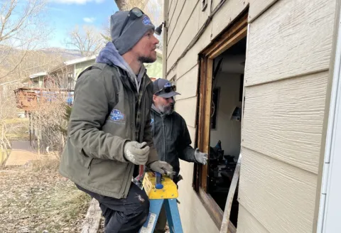 Two people replacing a window on a house