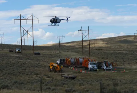 Helicopter and Black Hills Energy service trucks near transmission lines