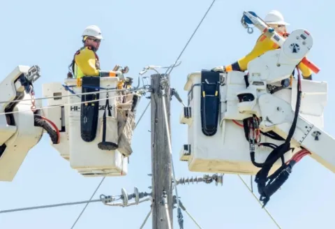 Linemen in buckets working at the top of a power pole